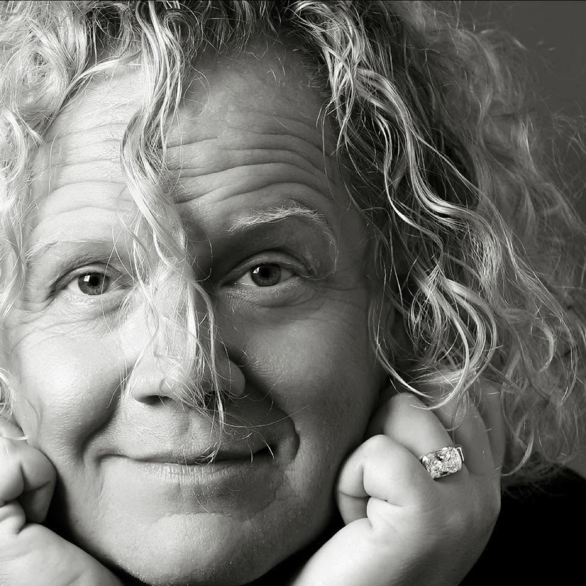 Black-and-white portrait of Taylor McLendon, curly hair falling over one eye, chin resting on his hands.